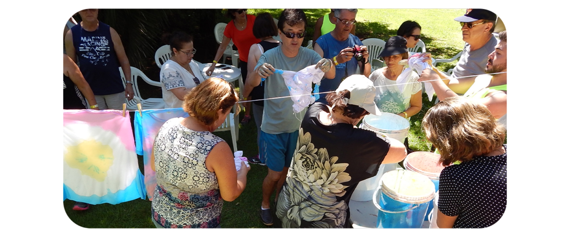 Grupo participa de oficina de tie-dye ao ar livre, tingindo camisetas com cores vibrantes no gramado do resort.