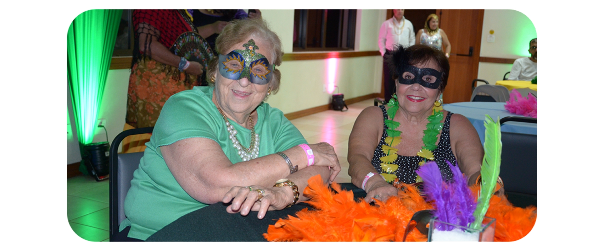 Duas senhoras com máscaras e adereços carnavalescos sorriem durante baile temático no Aguativa Resort.
