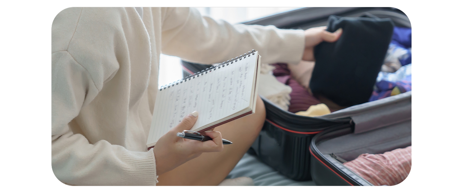 Pessoa anotando em caderno e organizando roupas em mala aberta para viagem.