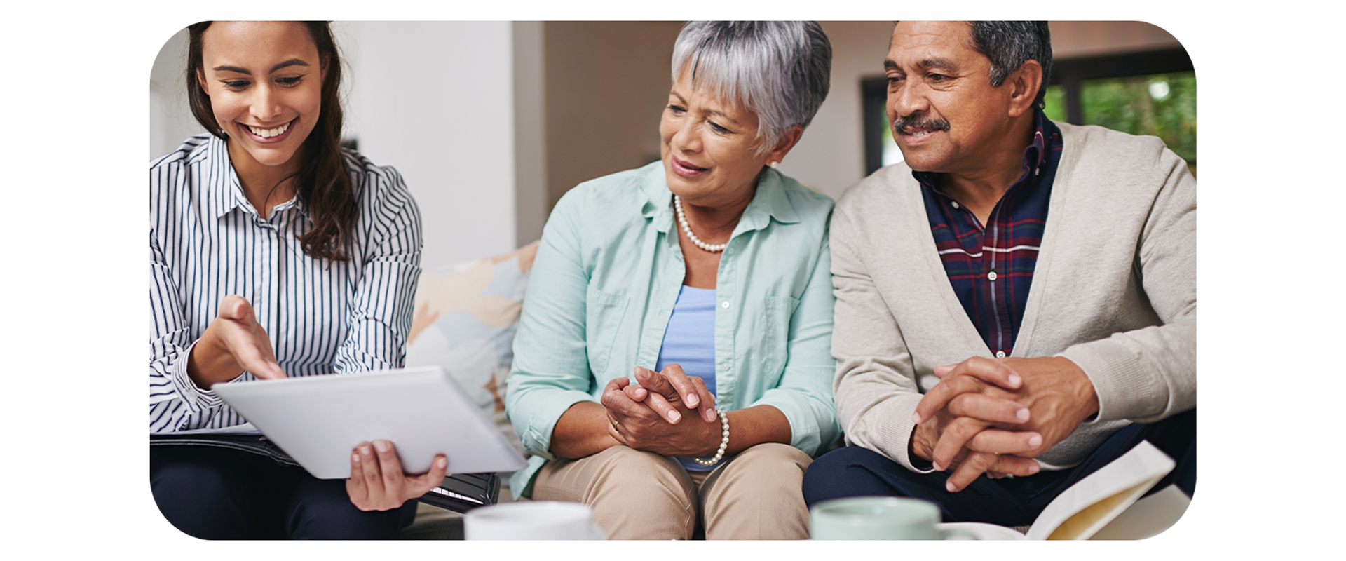 Agente de viagens mostra informações em tablet para casal de clientes sentados no sofá.