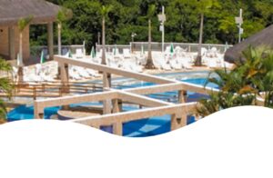 Vista aérea das piscinas e área de lazer do Aguativa Golf Resort, com espreguiçadeiras, palmeiras e quiosques ao fundo.