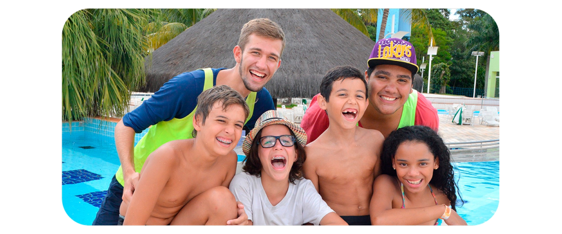 Crianças e monitores sorrindo e se divertindo juntos na área da piscina de um resort.
