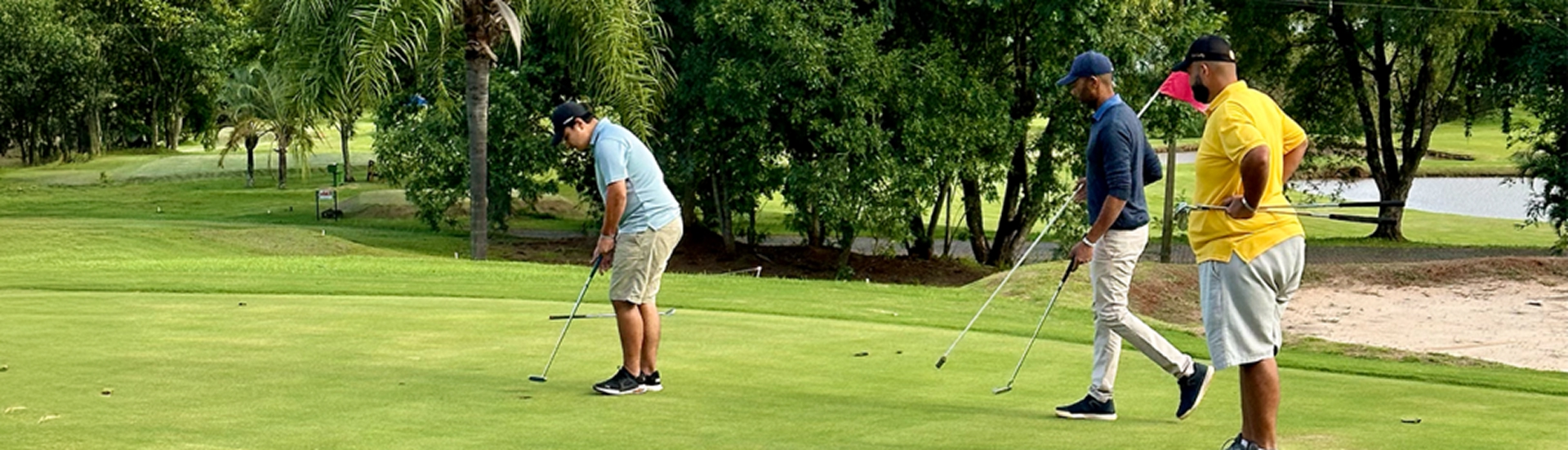 Quatro jogadores de golfe em campo, com um deles prestes a finalizar uma tacada no green, rodeados por árvores e vegetação ao fundo no Aguativa Golf Resort.